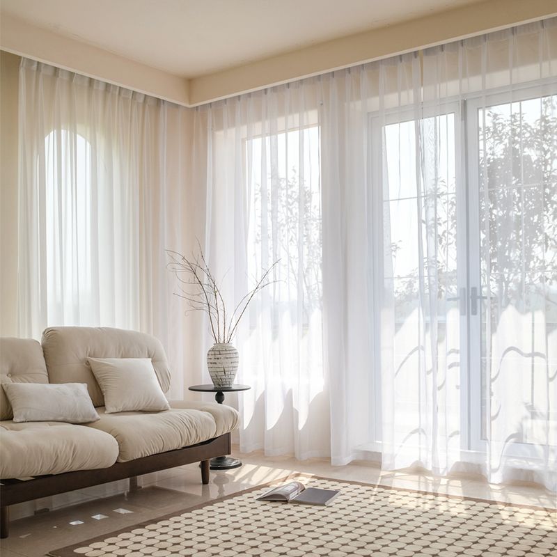 Sheer white curtain panels in a modern living room with natural light and a beige sofa.