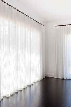 Sheer white curtains on black curtain tracks in a bright modern living room with dark floors