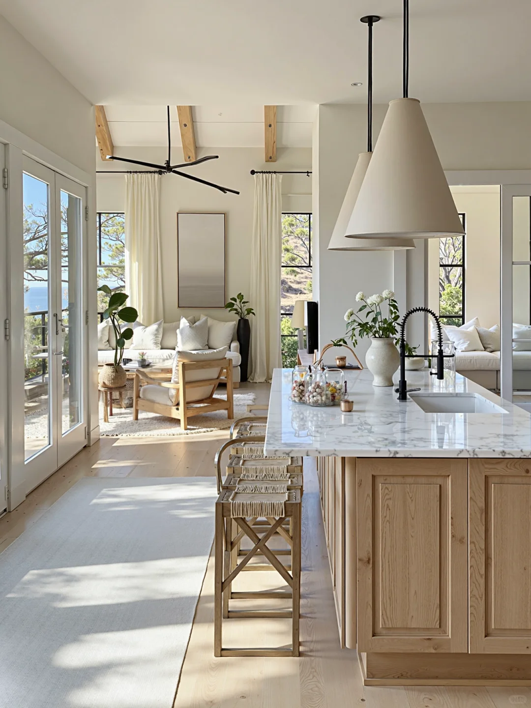Bright modern kitchen with marble island, light wood cabinets, and floor-to-ceiling cream curtains.