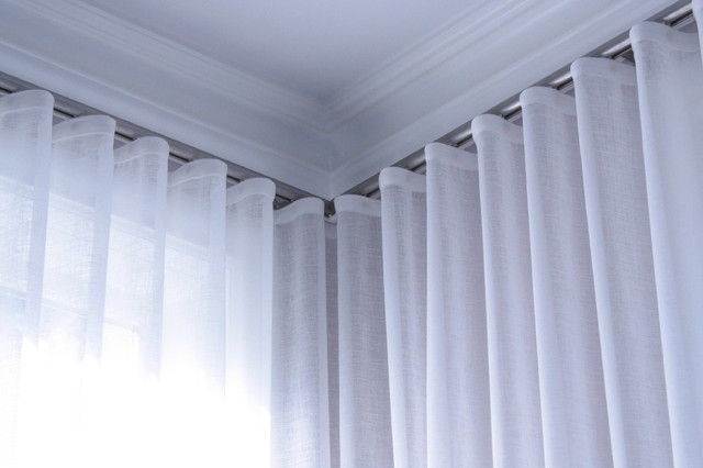 Sheer white curtains on ceiling-mounted corner track for modern living room window