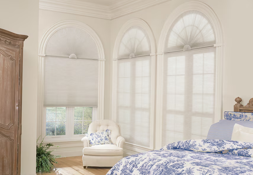 Bedroom with arched windows featuring white blackout curtain shades, armchair, and cozy bedding.