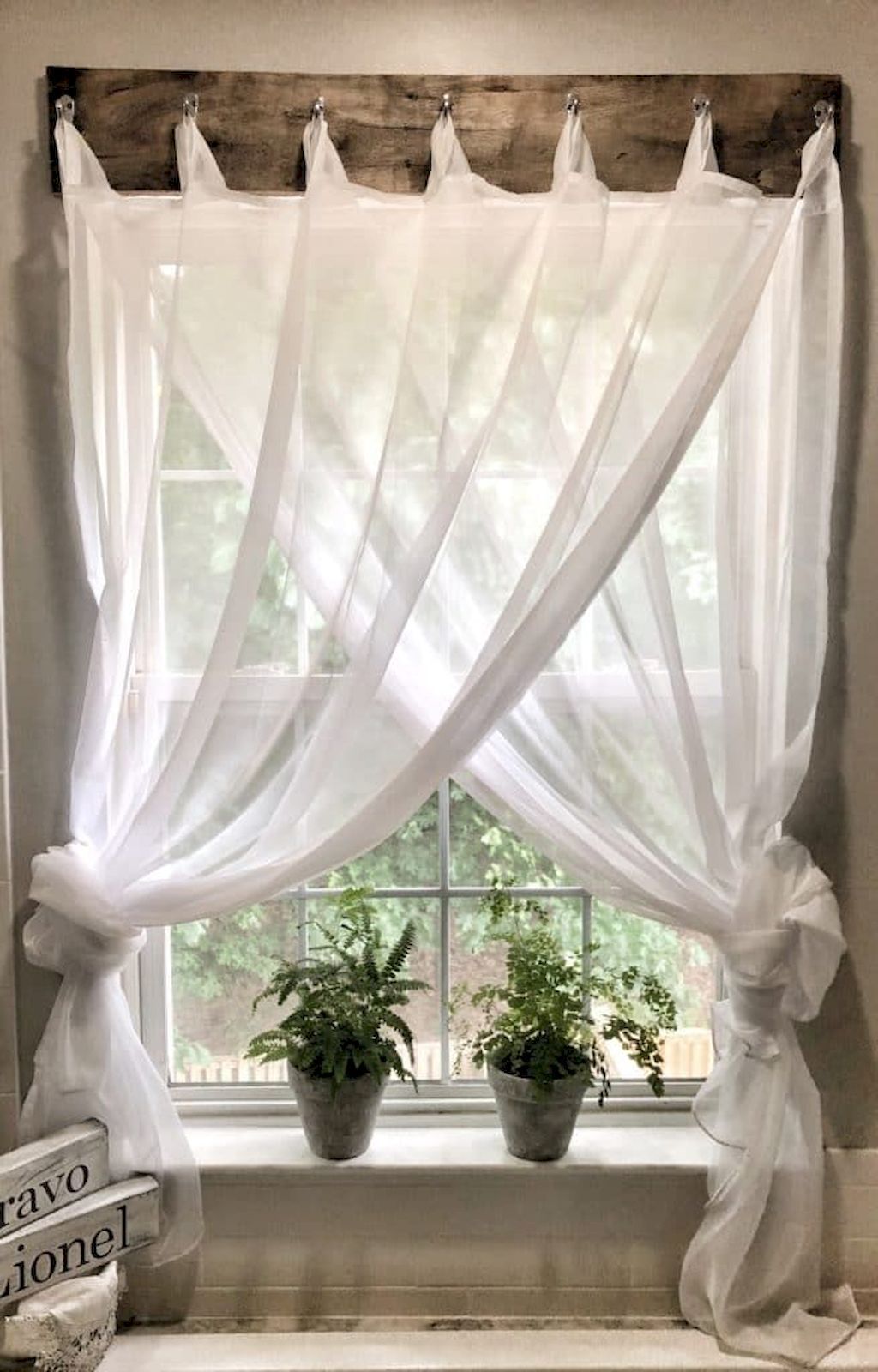 DIY-friendly sheer curtain panels on rustic wood track above window, potted plants on sill