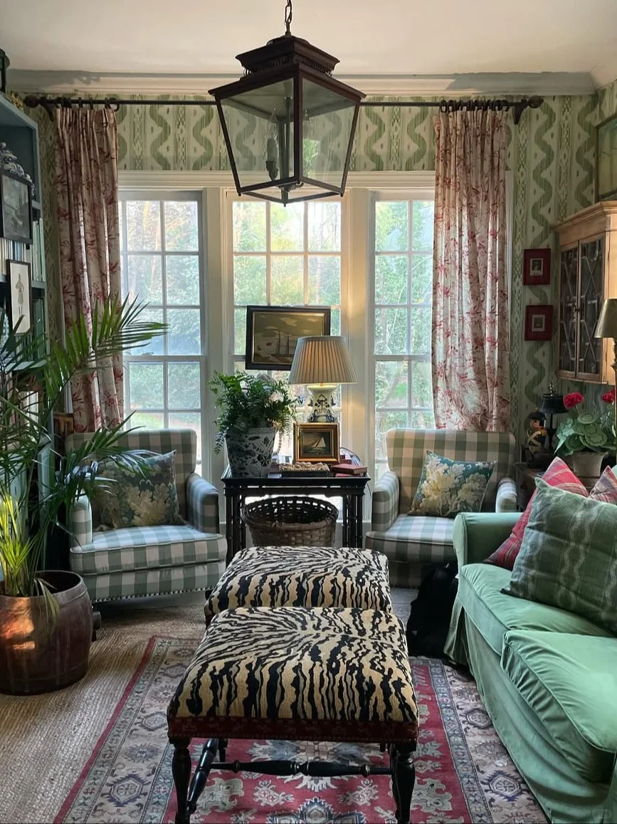 Cozy living room with large windows, patterned curtains, green sofa, striped armchairs, and animal print ottomans.