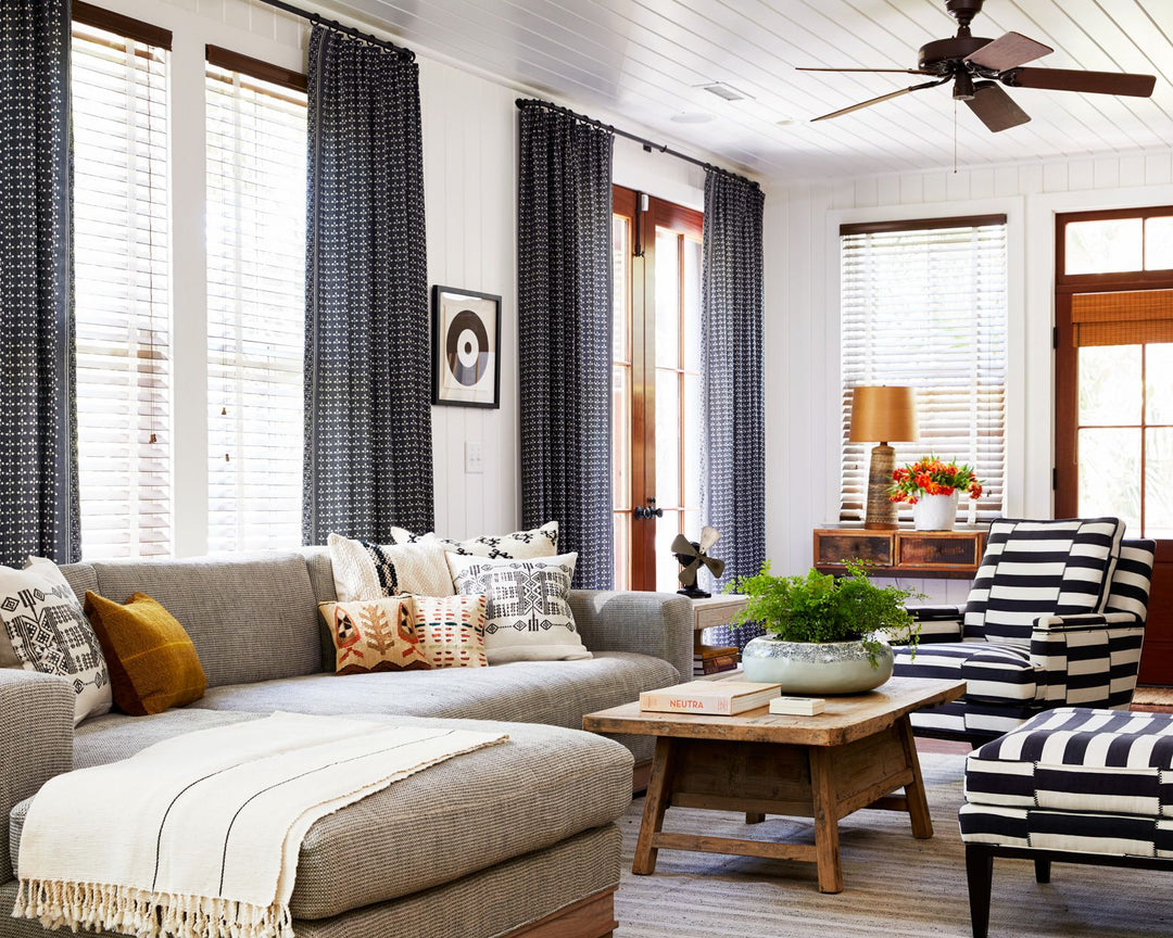 Modern living room with patterned blackout curtains, striped armchair, sectional sofa, and wooden coffee table.
