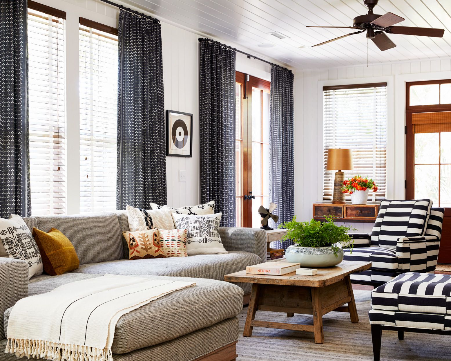Modern living room with patterned blackout curtains, striped armchair, sectional sofa, and wooden coffee table.