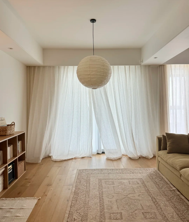 Modern living room with floor-to-ceiling sheer curtains, beige sofa, and paper pendant light