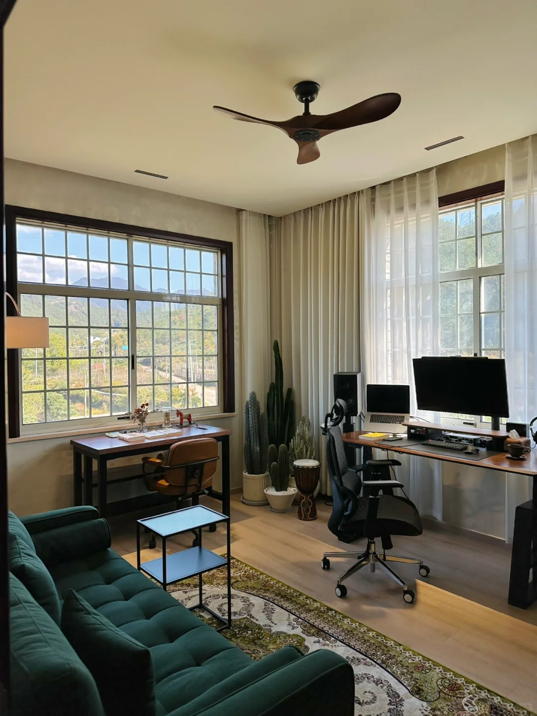 Modern home office with sheer white curtains, large windows, desk, and green sofa