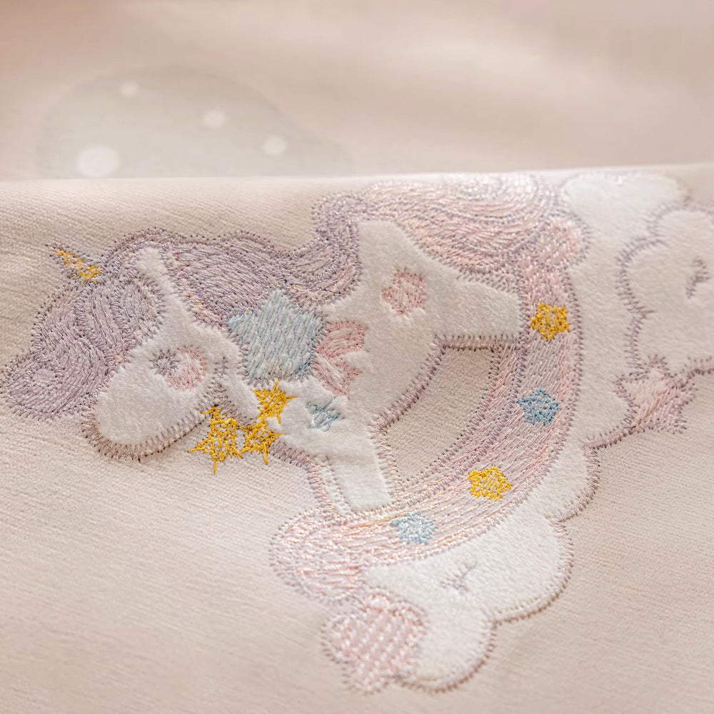 Close-up of pastel embroidered unicorn on soft fabric with stars and clouds pattern