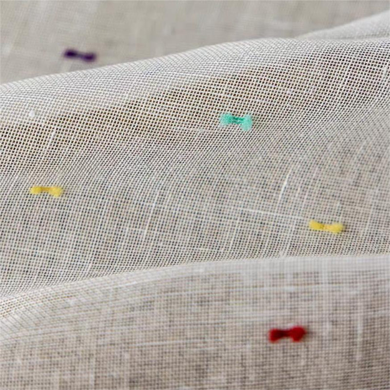 Close-up of sheer curtain fabric with colorful embroidered dots and neutral background